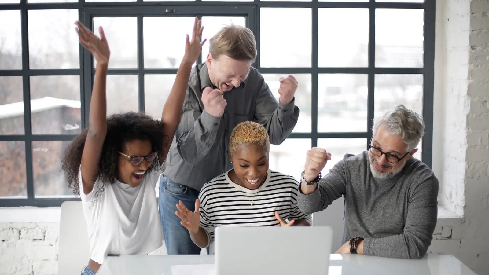 Sales and marketing teammates cheering around a laptop as a deal closes