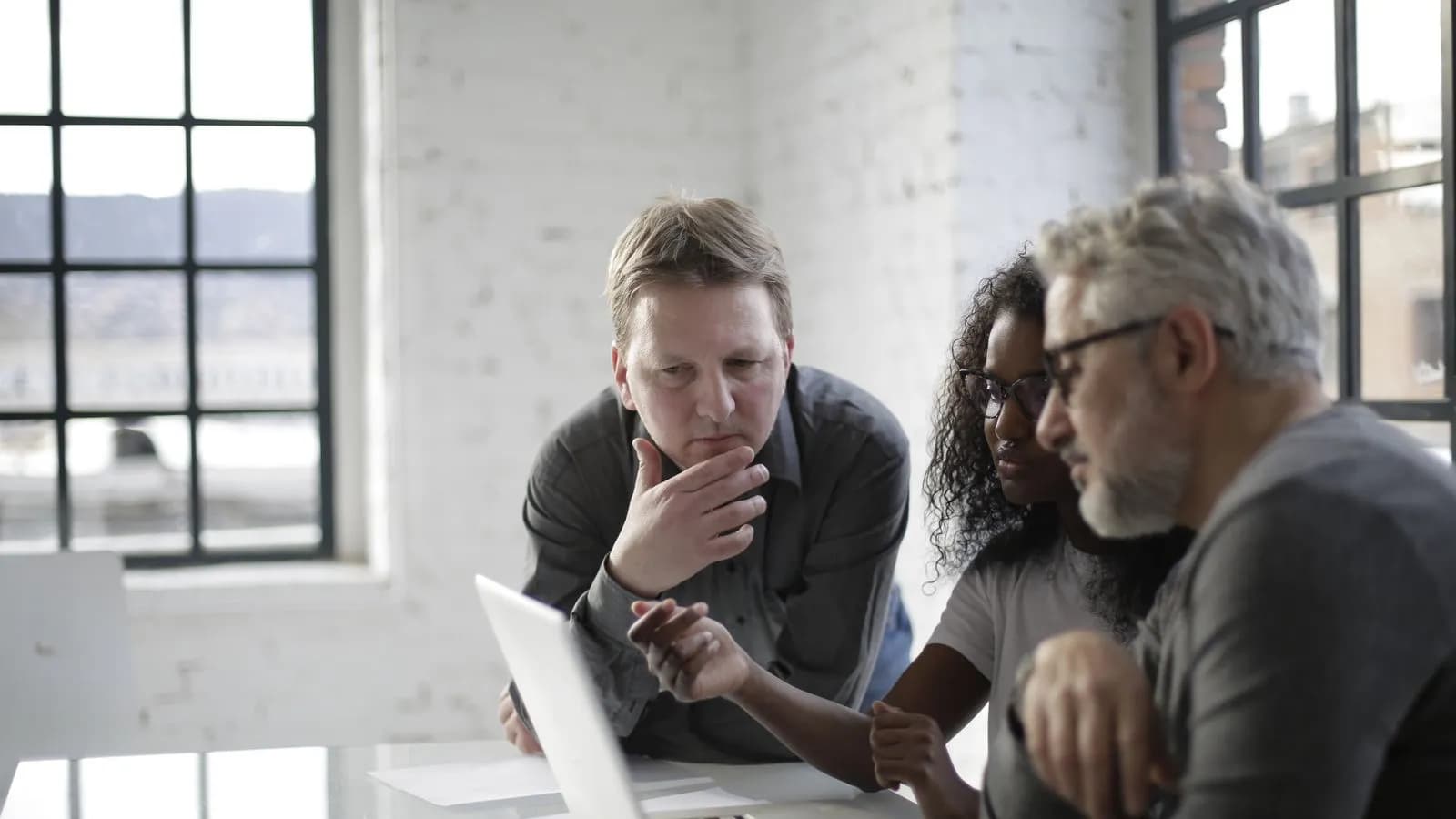 Three colleagues huddled around a laptop, quietly evaluating vendor options in a private meeting