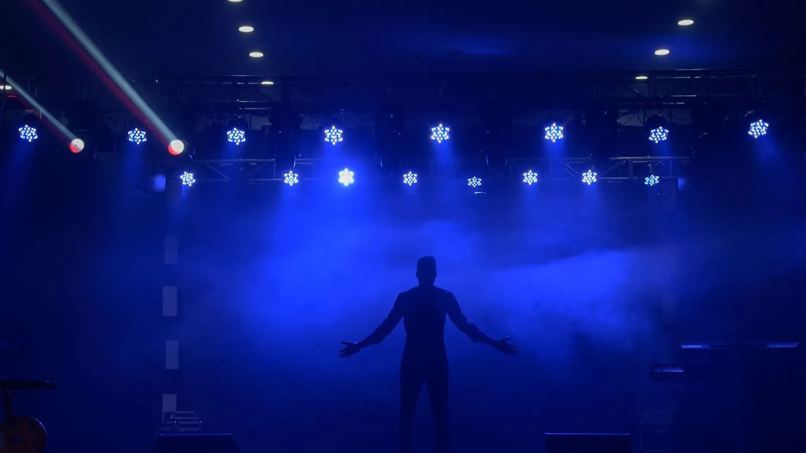 Lone silhouetted figure emerging from darkness under blue stage lights, evoking anonymous buyer intent coming into focus