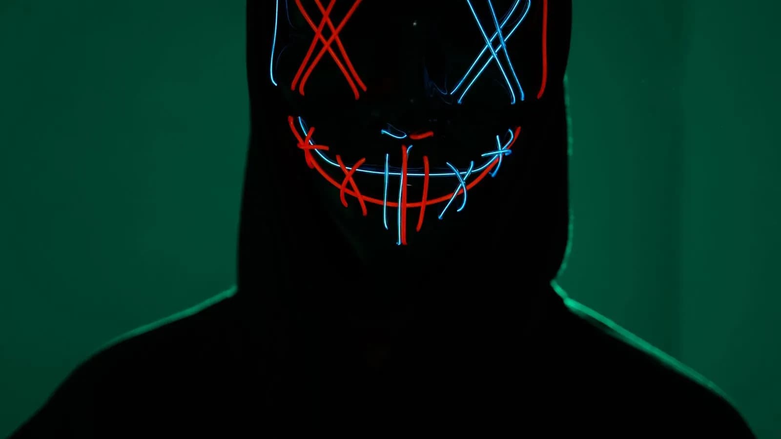 Anonymous hooded figure wearing a glowing neon mask in the dark, representing ad fraud and invalid bot traffic