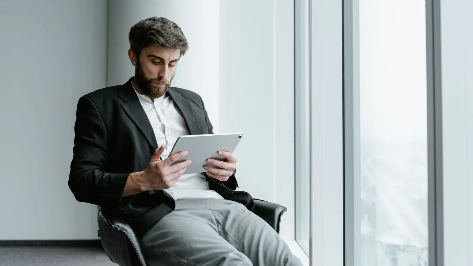 A B2B buyer researching options alone on a tablet beside a large office window before contacting sales