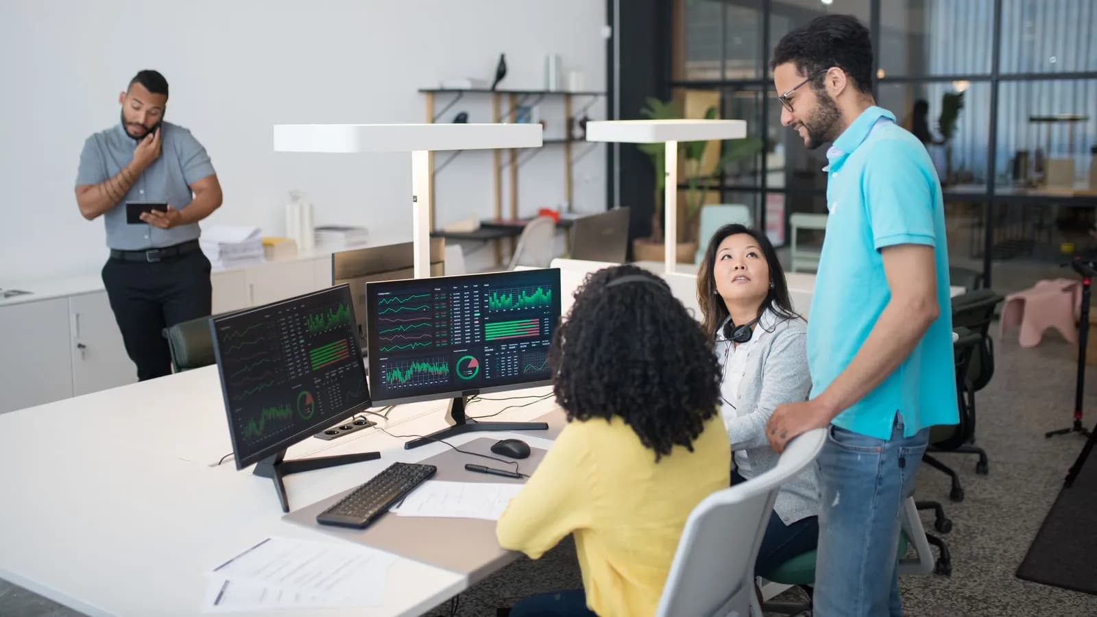 Team in a bright modern office collaborating around monitors displaying revenue analytics dashboards