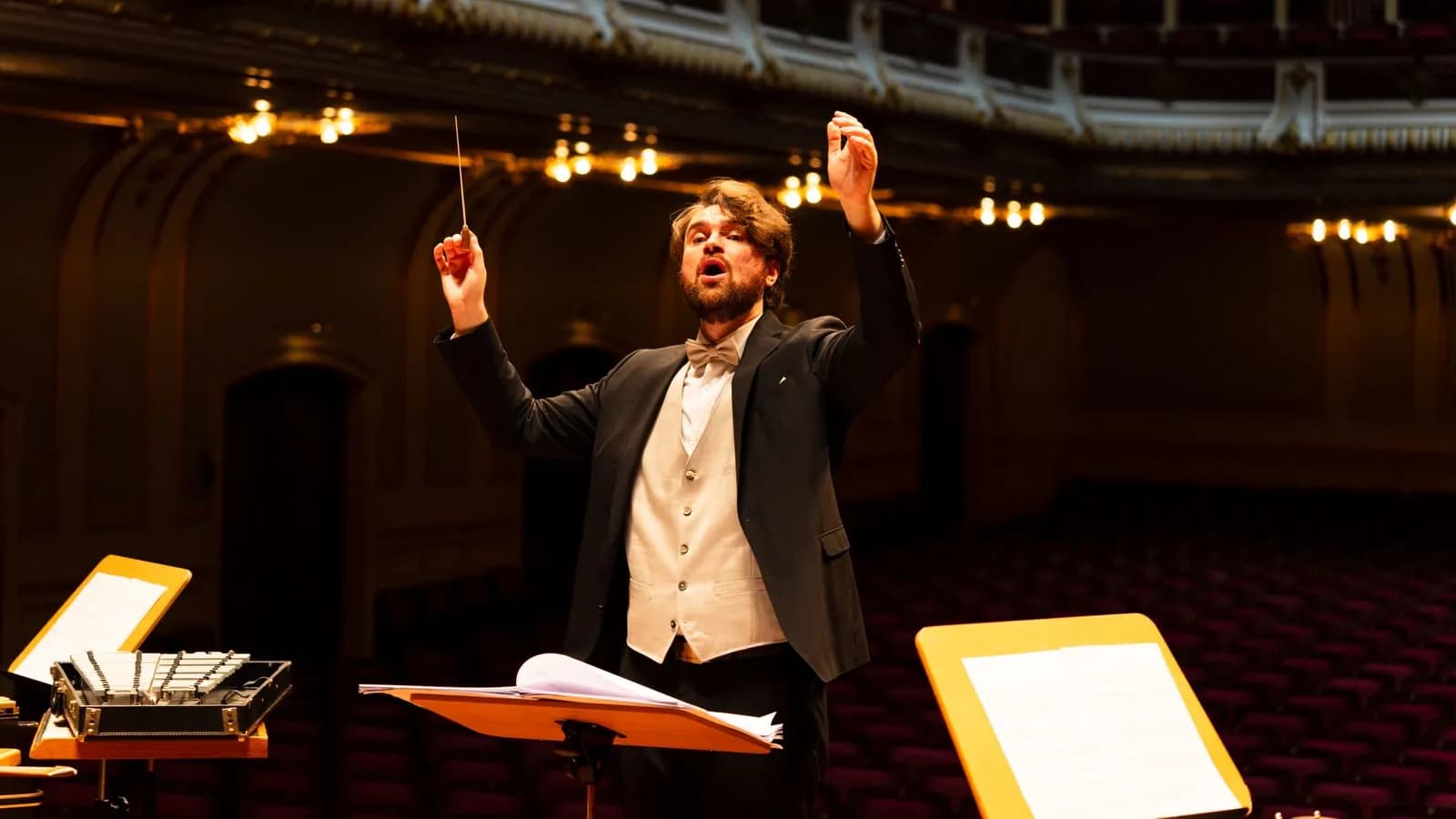 Orchestra conductor mid-performance with baton raised, orchestrating every section as one system