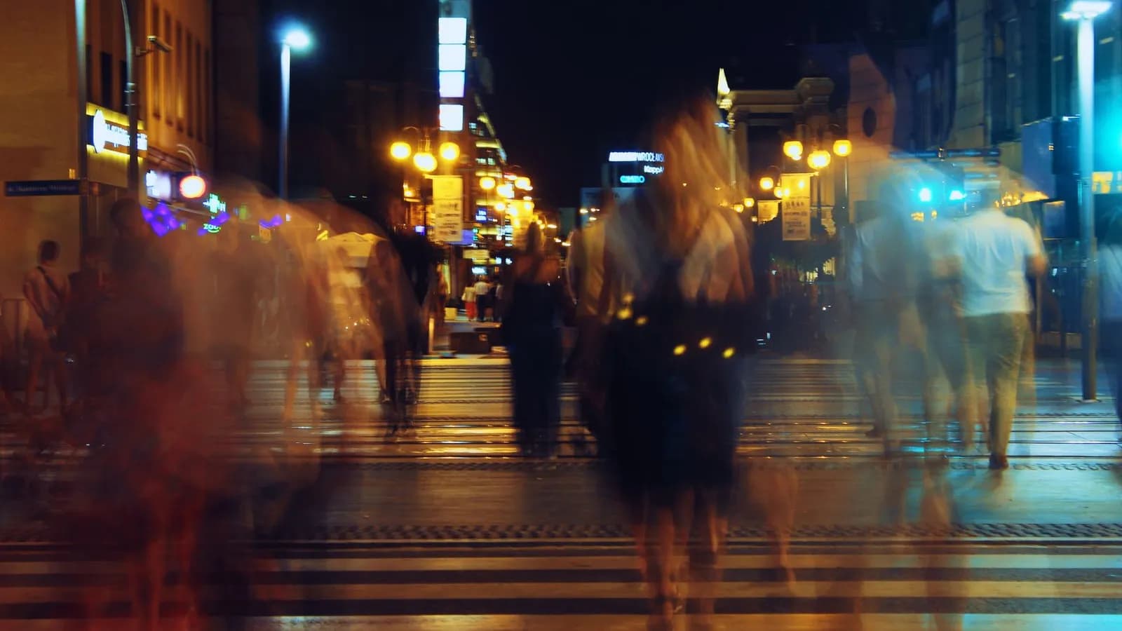Blurred stream of anonymous pedestrians crossing a city street at night — the buyers you never see