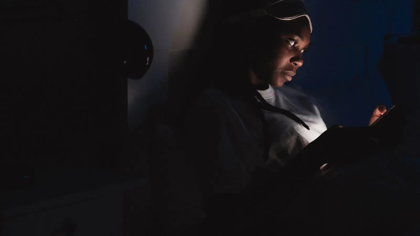 A buyer researching vendors alone at night, face lit only by a device screen in a dark room