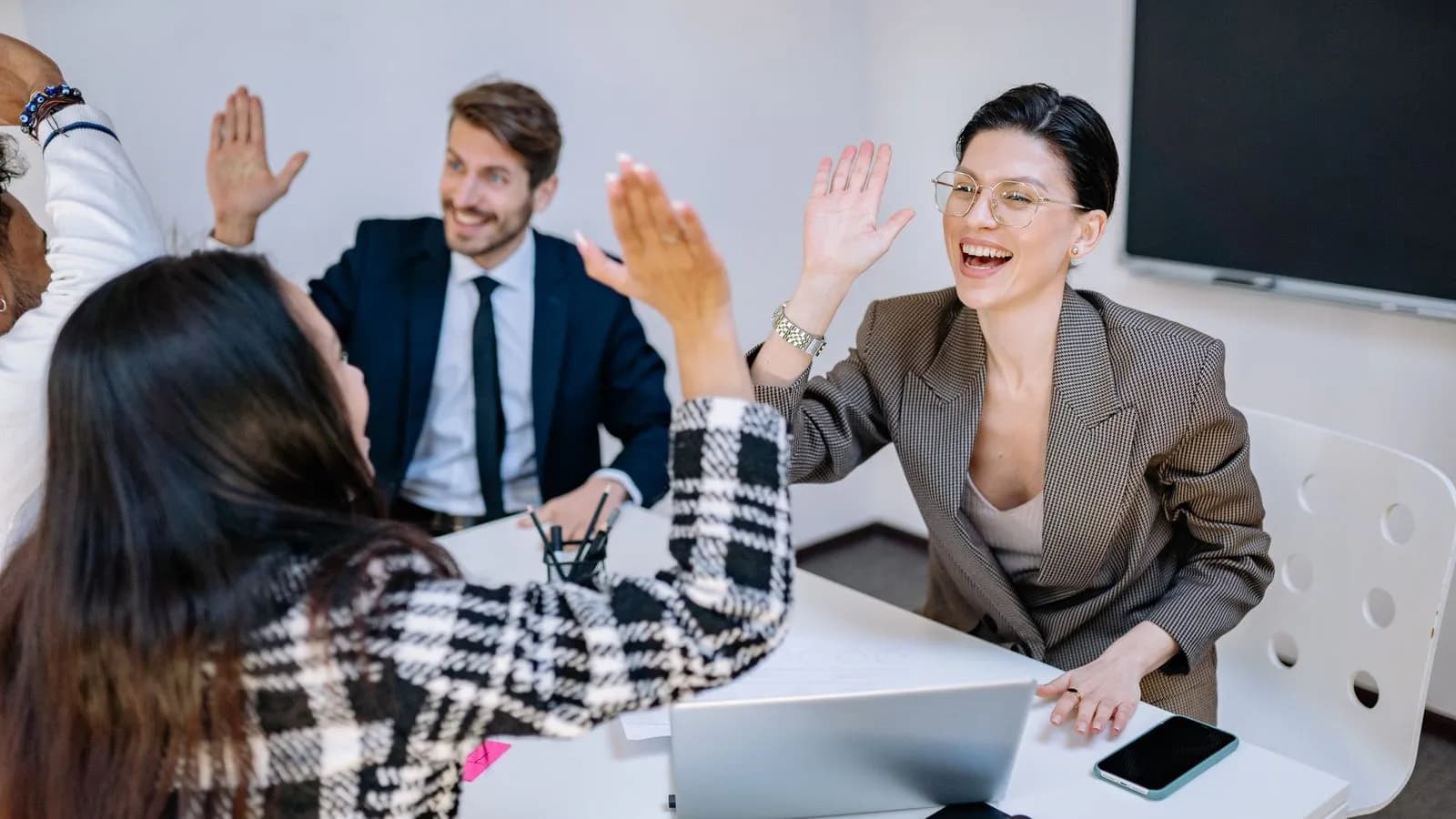 Business team exchanging high fives around a meeting table, celebrating a partnership win